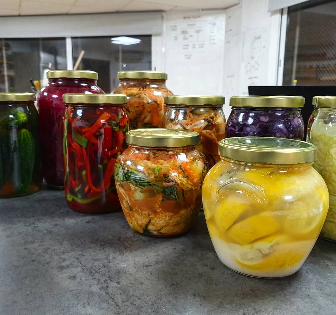Conjunto de frascos con pepinos, kimchi, col lombarda, chucrut y limones fermentados sobre la mesa del aula