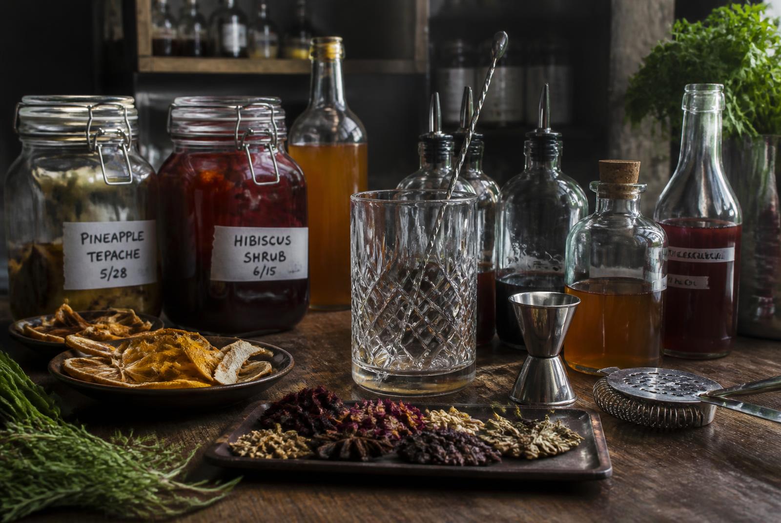 Estación de trabajo de coctelería fermentada: tarros de tepache y shrub, botellas, vaso mezclador y botánicos secos