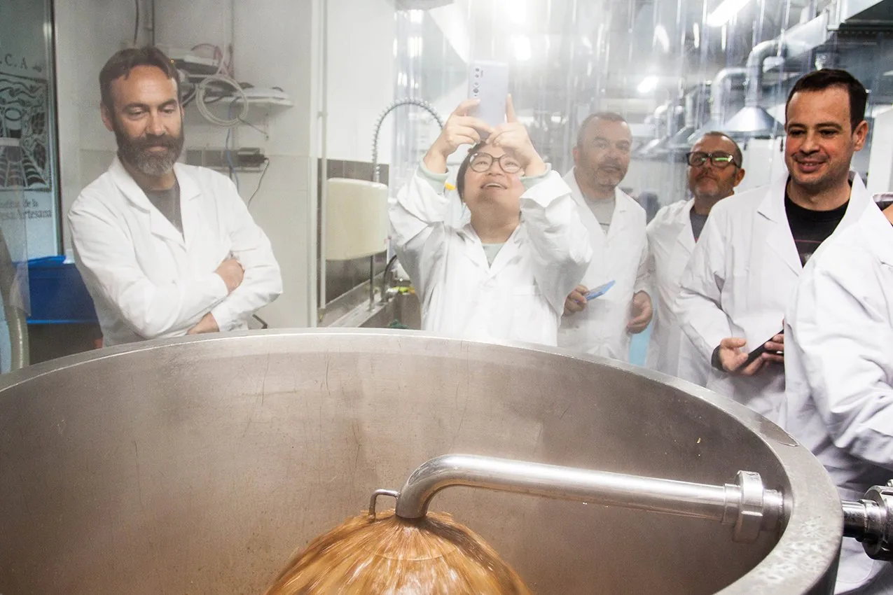 Adición de lúpulo a la olla de cocción entre vapor, con alumnos observando