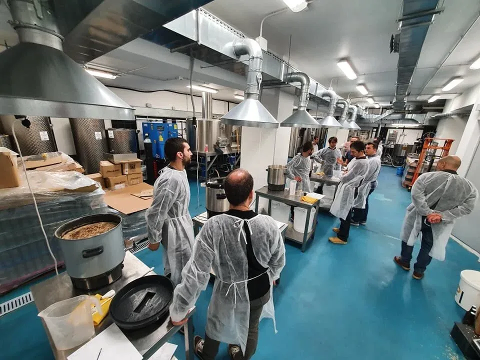 Alumnos con bata trabajando en la sala de elaboración durante un curso de cerveza todo grano